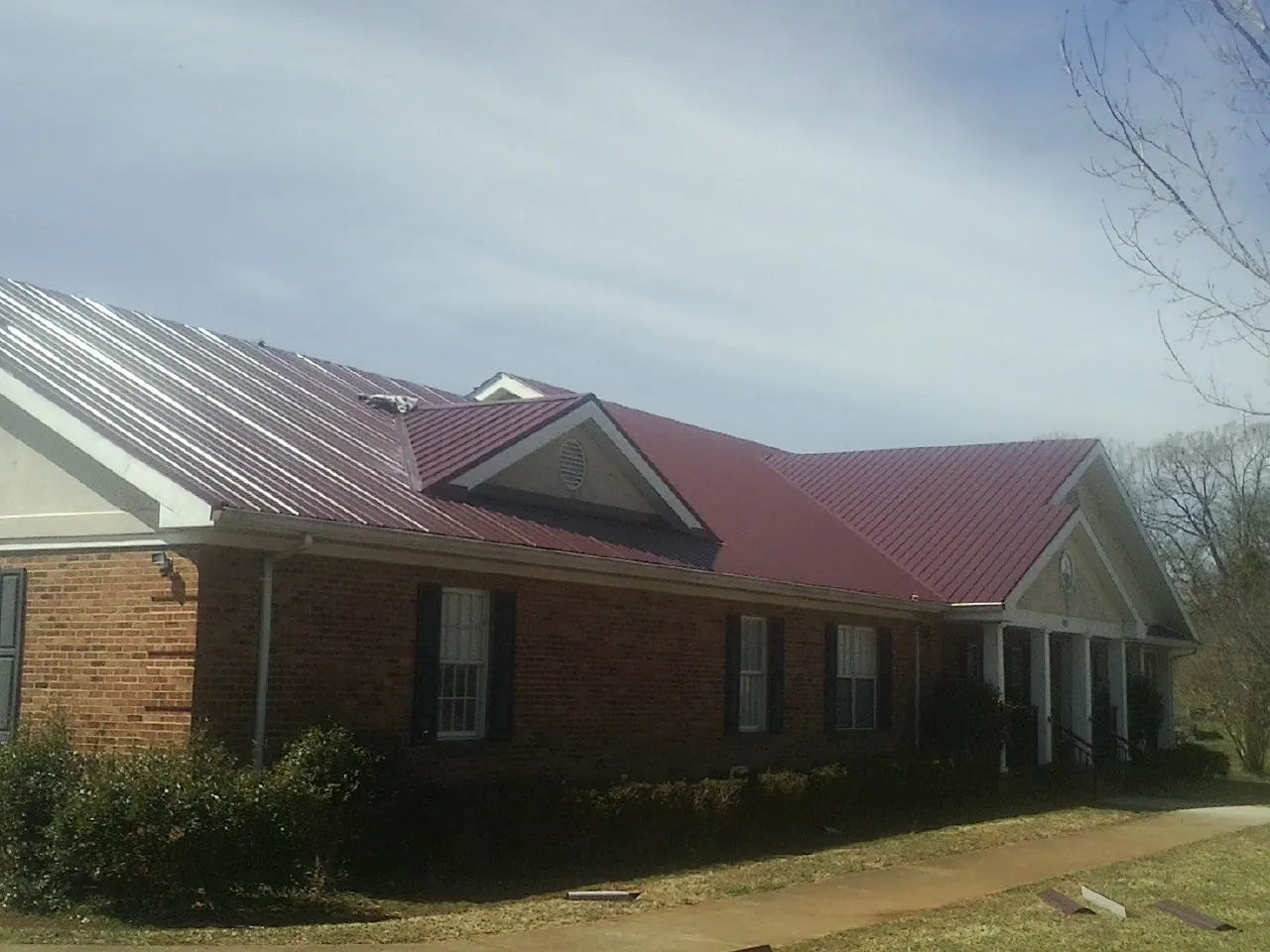 Red metal roof with gabled entries on a long brick building, from a Hail Damage Roof Repair job in Walling