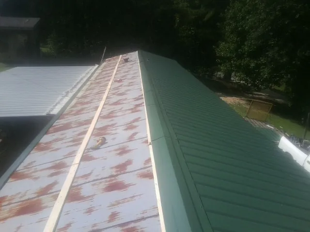 Old rusted panels beside newly installed green metal roofing — Wind Damage Roof Repair by Roofing Brothers in Walling