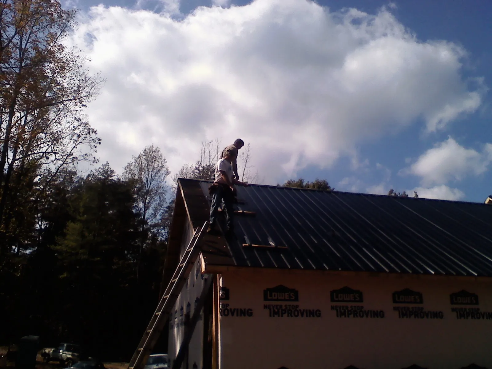 Roofer fastening dark metal panels high against a cloudy sky, from a Roof Inspection job in Walling